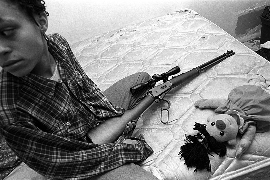 A woman with a gun and a doll on a mattress.
