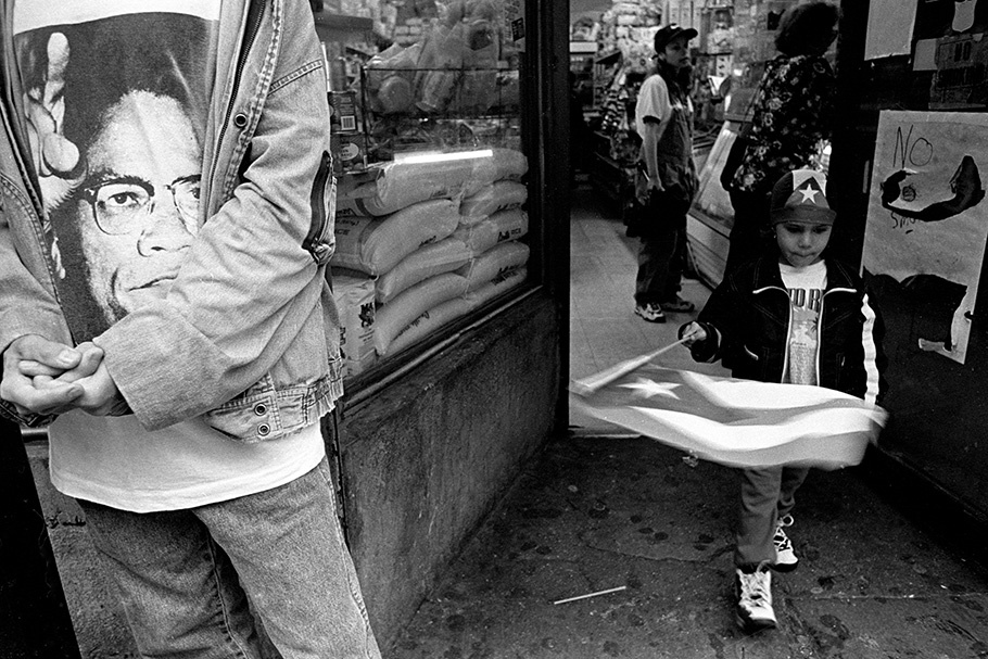 A child with a flag next to someone in a Malcolm X T-shirt.