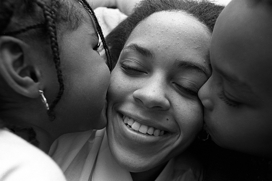 Two children kissing a woman’s cheeks.
