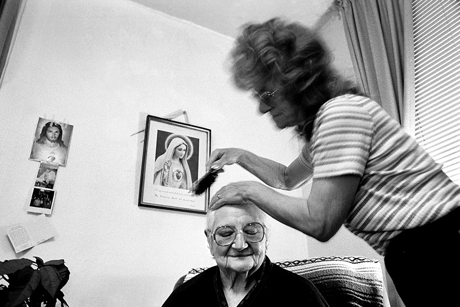 A caregiver brushes an elderly woman’s hair.