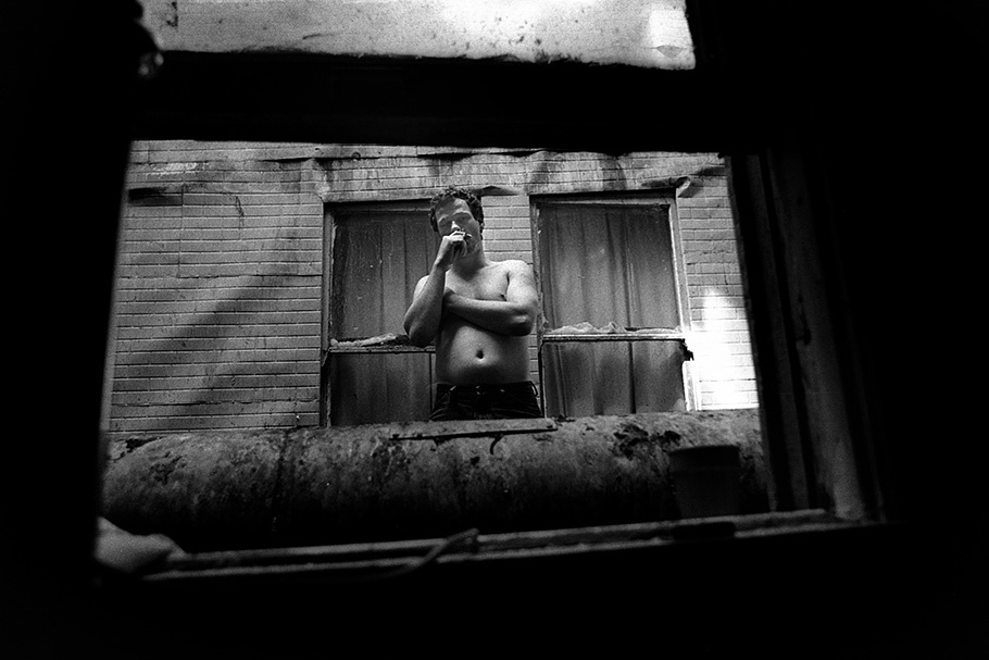 A shirtless man viewed through a window.