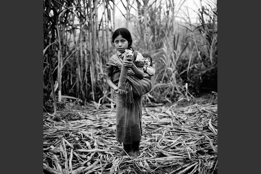 A girl with a baby on her back, holding a mortar shell.