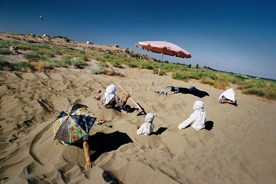 Women with headscarves sitting in sand.