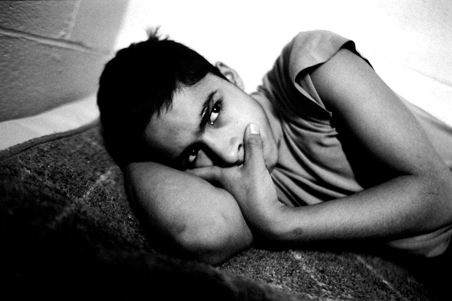 A boy lying on the floor of a cell with a look of anger.