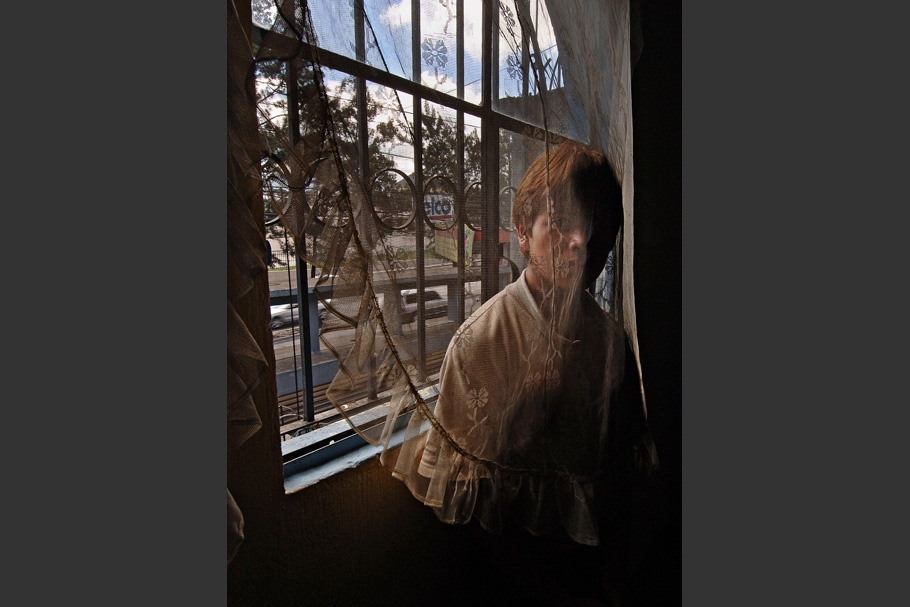 A teenager in a window behind a lace curtain.