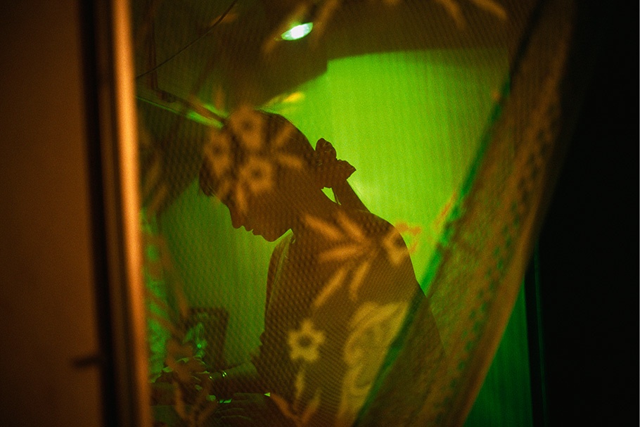 A woman silhouetted between lace and a green wall.