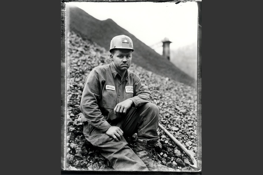 A miner sitting on a hill wearing a hard hat.