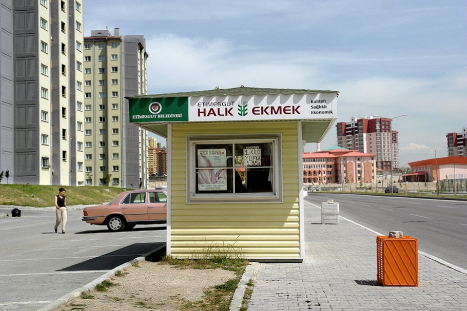 Yellow booth (“Halk Ekmek”) in foreground, car and buildings in background.