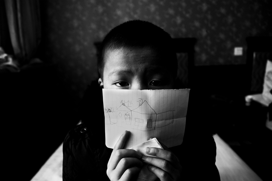 A young boy holds a piece of a paper in front of his face.