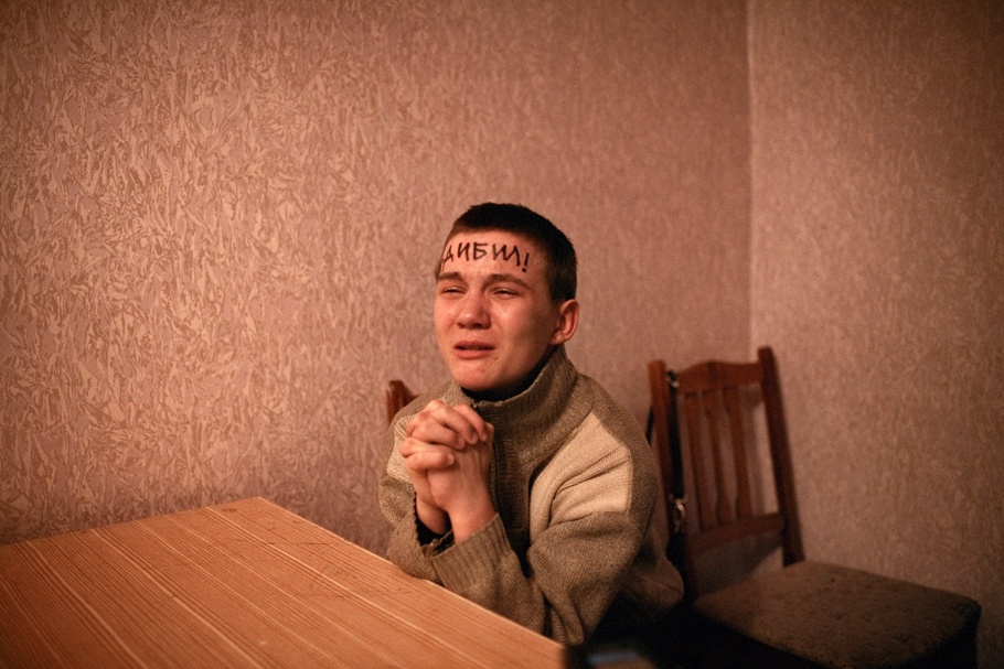A young boy crying with clasped hands and words written on his forehead.