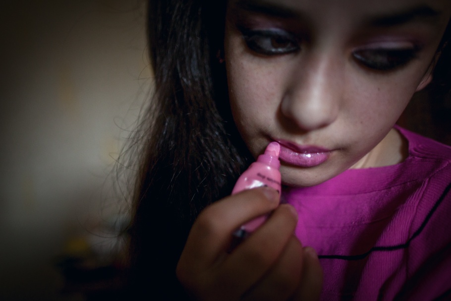 A young girl puts on lip-gloss