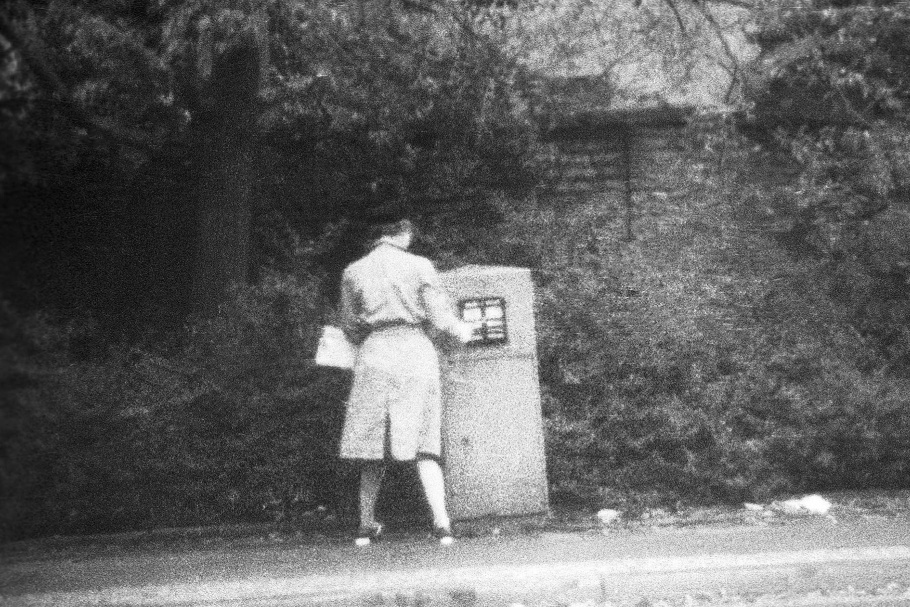 Woman with trench coat and black hat placing mail in mailbox