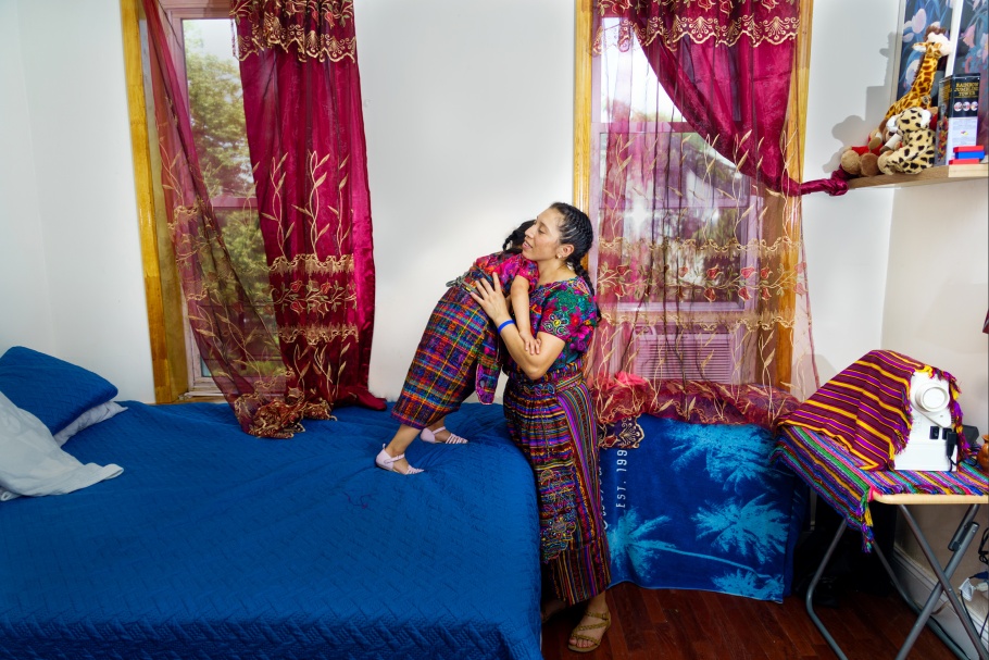 A woman hugging a child who is standing on a bed