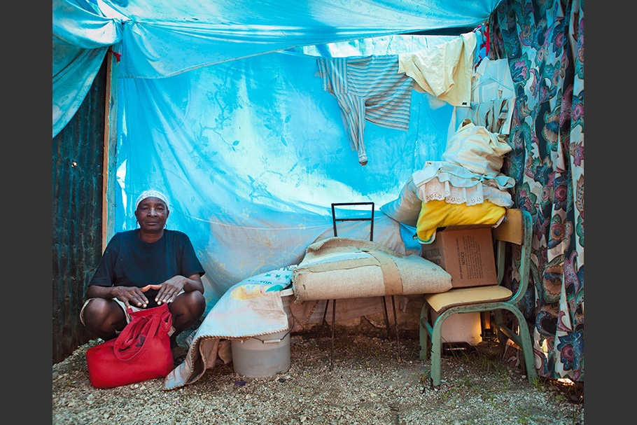 Woman sitting in tarp-covered home with possessions.
