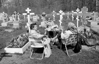 Three women sitting in lawn chairs in a cemetery.